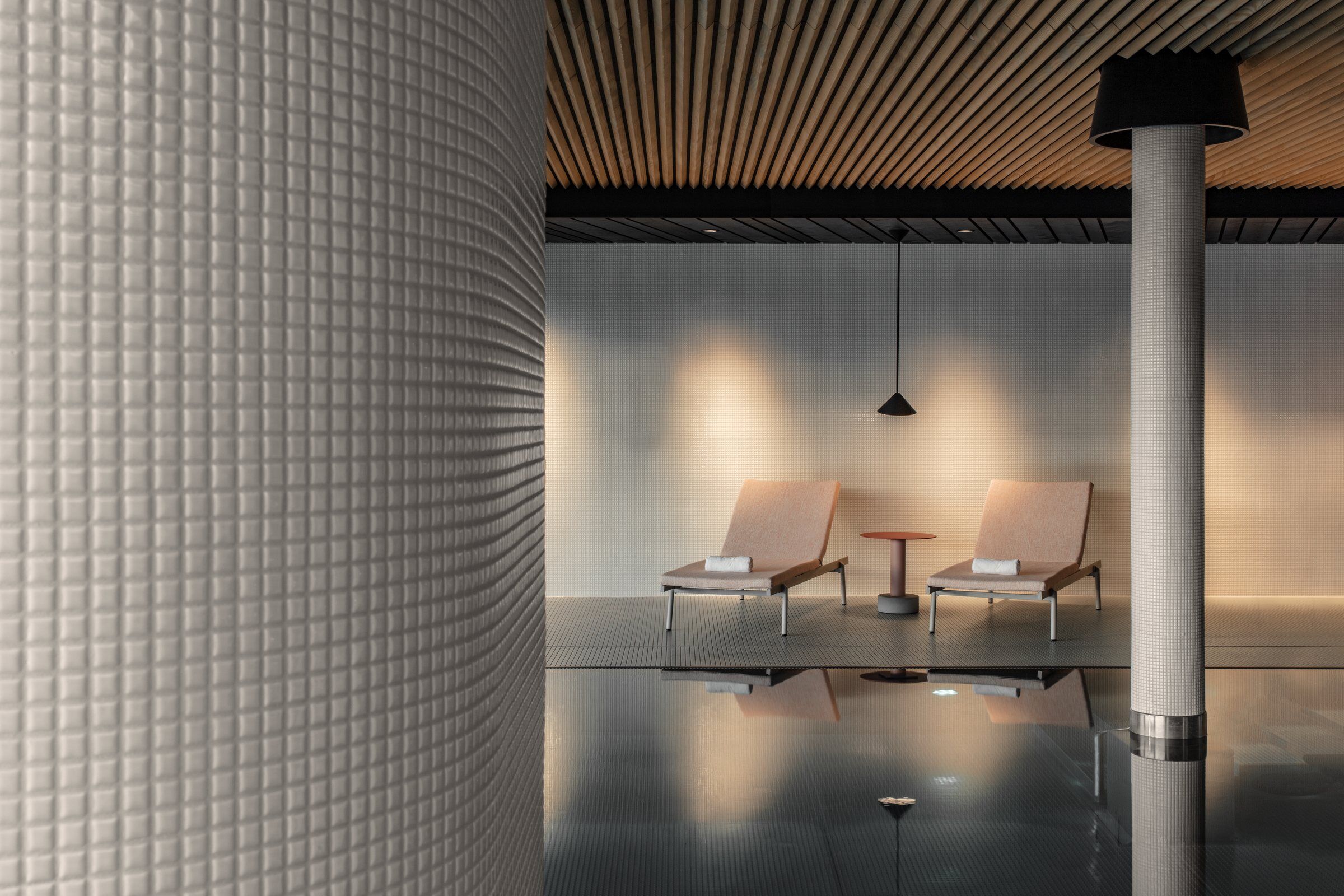 Swimming pool area - Appiani mosaic gloss tiles covered columns. Acoustic ceiling in spruce wood. Dropped ceiling black wood stained planks. Rail sunbeds by Pedrali. Roll side table by Patricia Urquiola for Kettal. Nod suspended light by XAL.