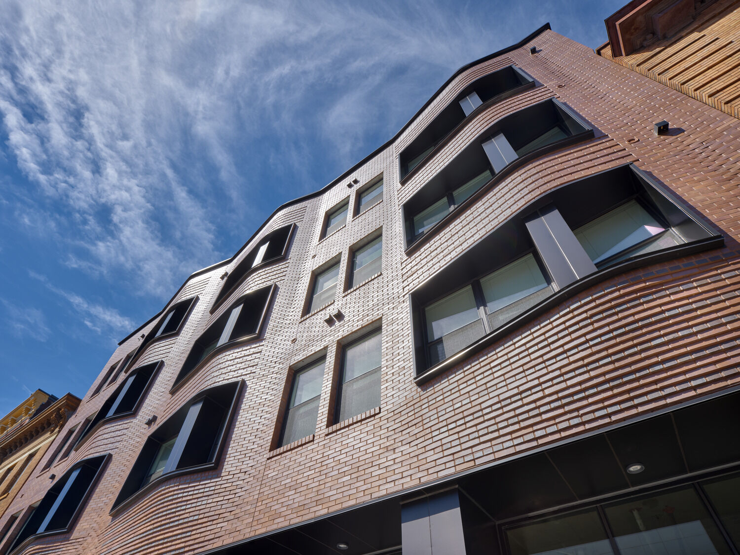 A modern take on the neighborhood’s historic oriels, Willkommen on Vine’s undulating brick wall gloats above a glass storefront, providing residents with privacy and sunlight.