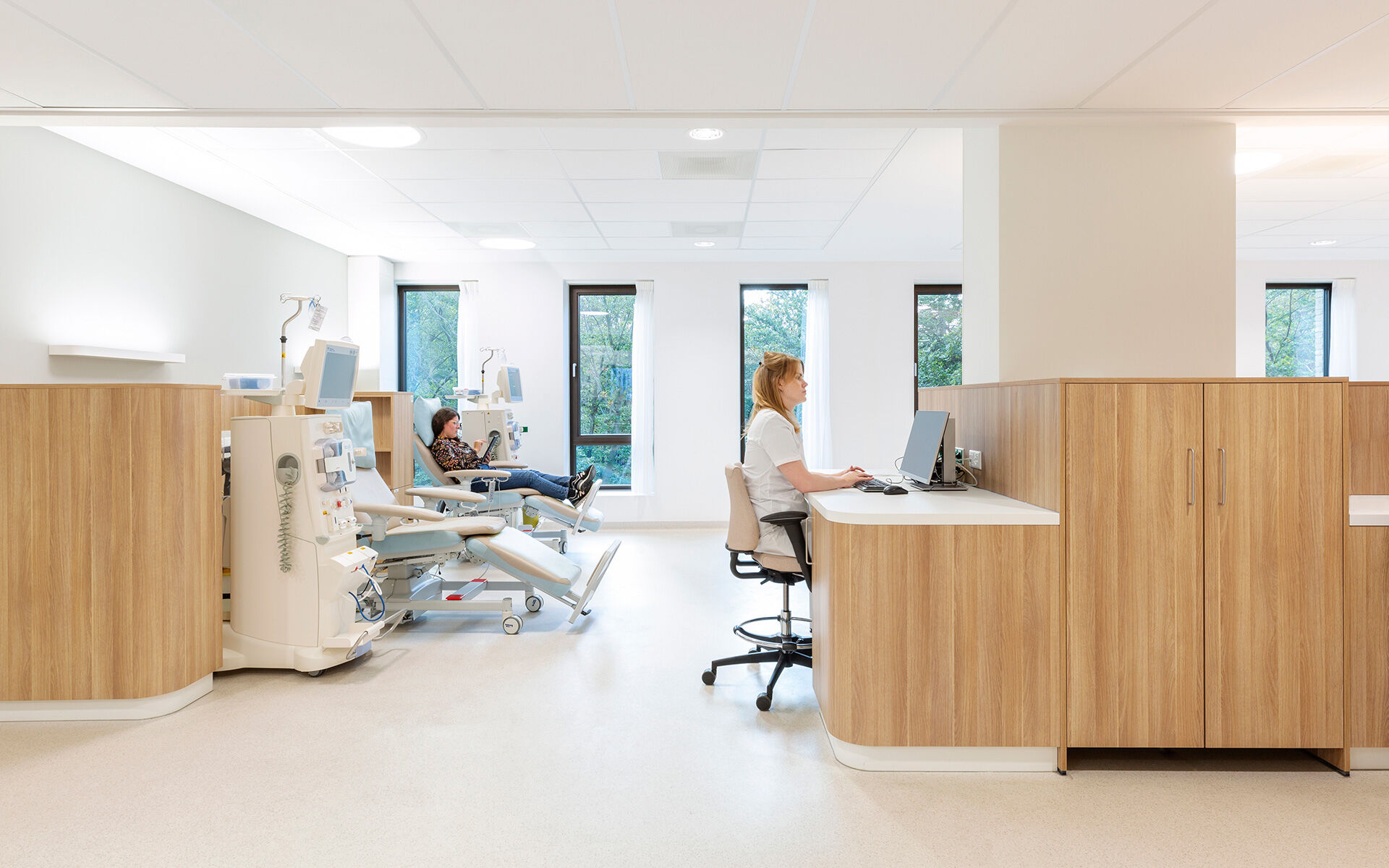 A spacious dialysis room with large windows on the wooded area