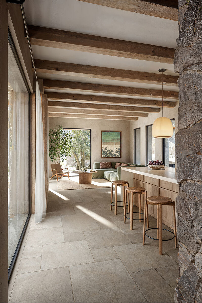 Interior view of the open-plan kitchen and living area, combining natural textures, timber beams and soft Mediterranean light.