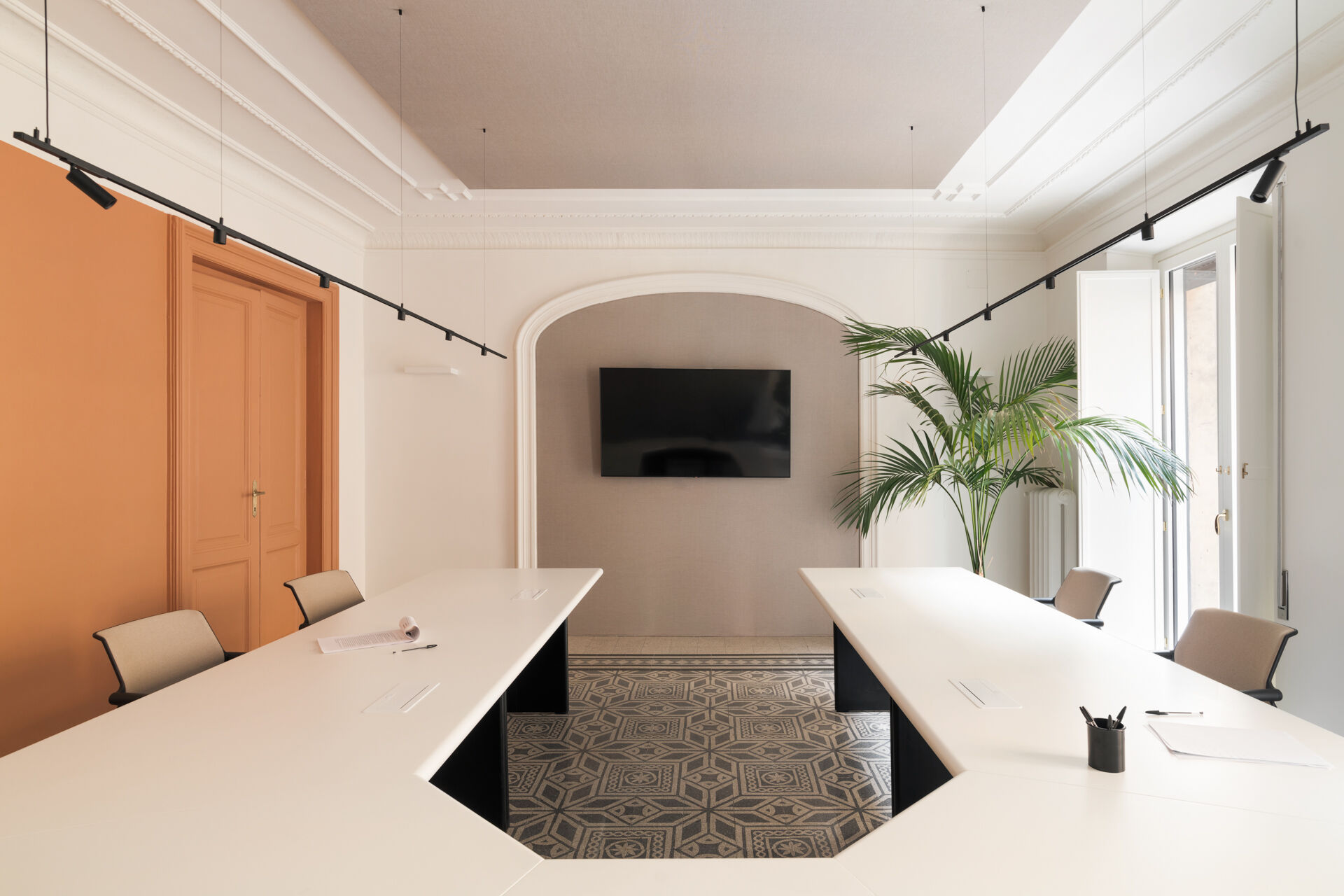 The meeting room is structured along a central axis ending in the existing arch, used as a backdrop. The solid color at the side threshold introduces the project’s chromatic system, while the table and linear lighting guide the space.