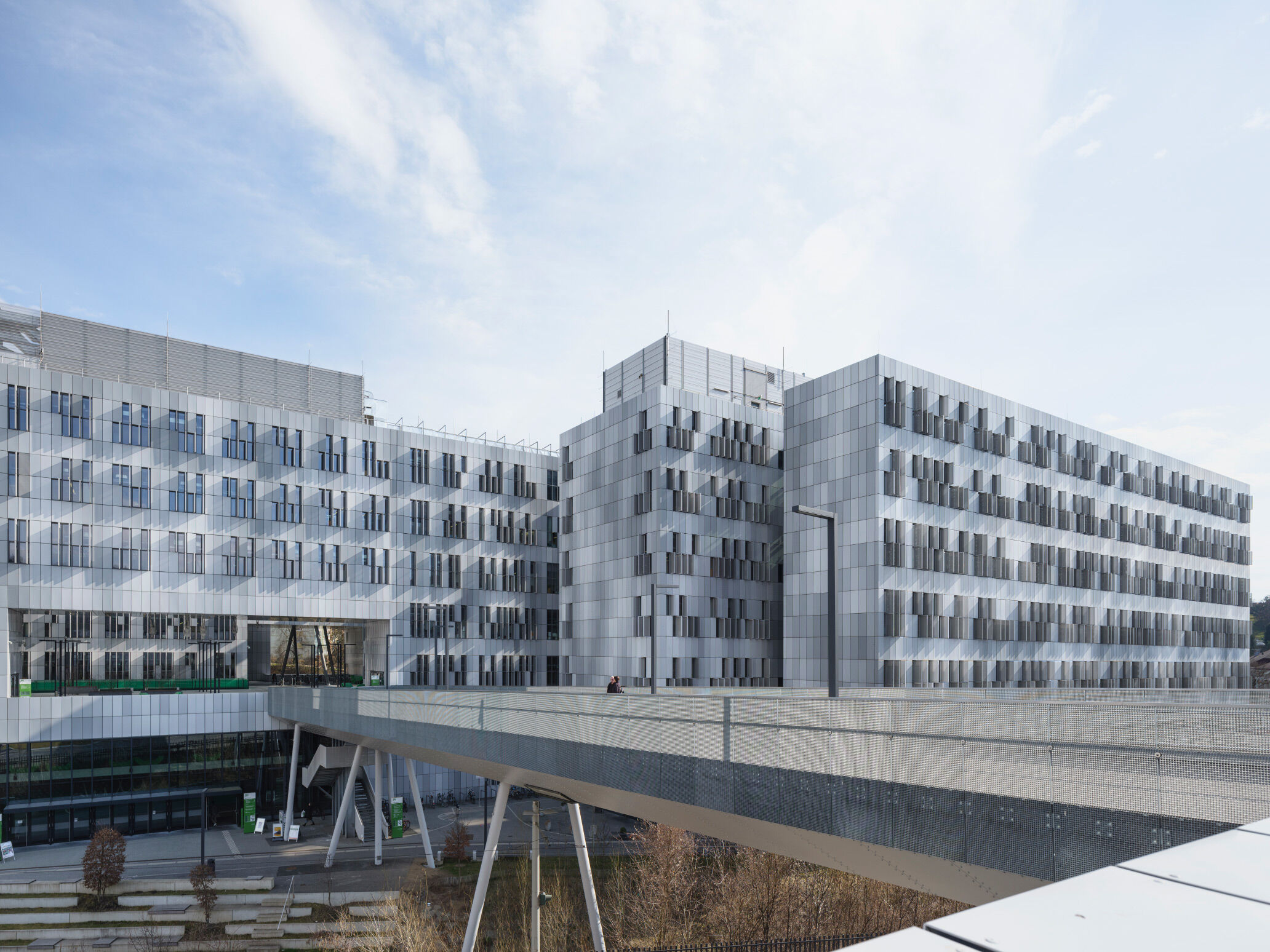 The east front of the complex, where a bicycle and pedestrian bridge spans both the Neue Stiftingtalstrasse and a watercourse to integrate the new site with existing university buildings.