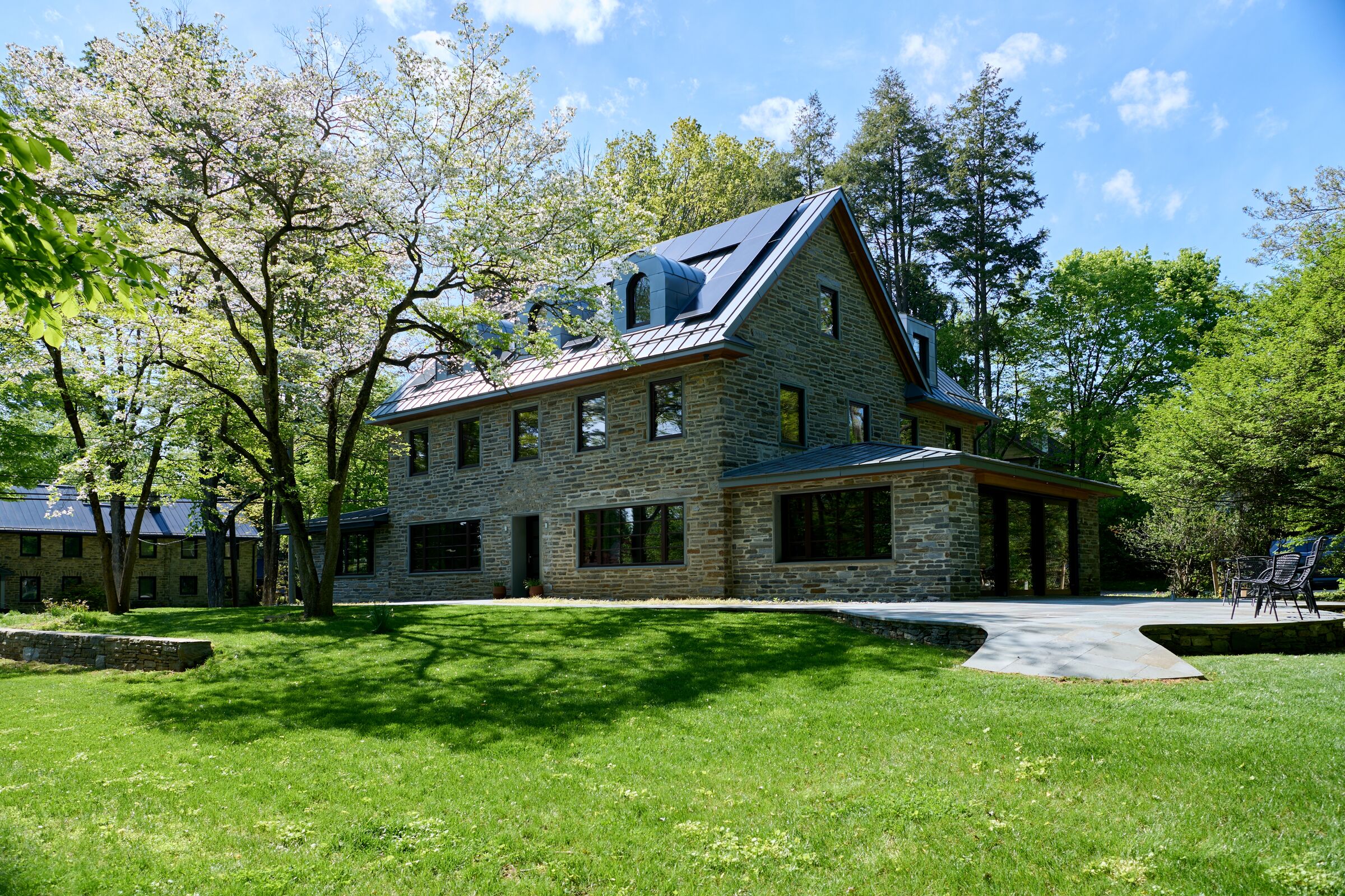 Accessible Masonry Gut Renovation - Exterior. Original Home - Horace Trumbauer, 1922.  Center high gabled area from original house. New stone additions. Zero-step entry doors. Bluestone hardscape with accessible ramps to all doors, street and lawn.