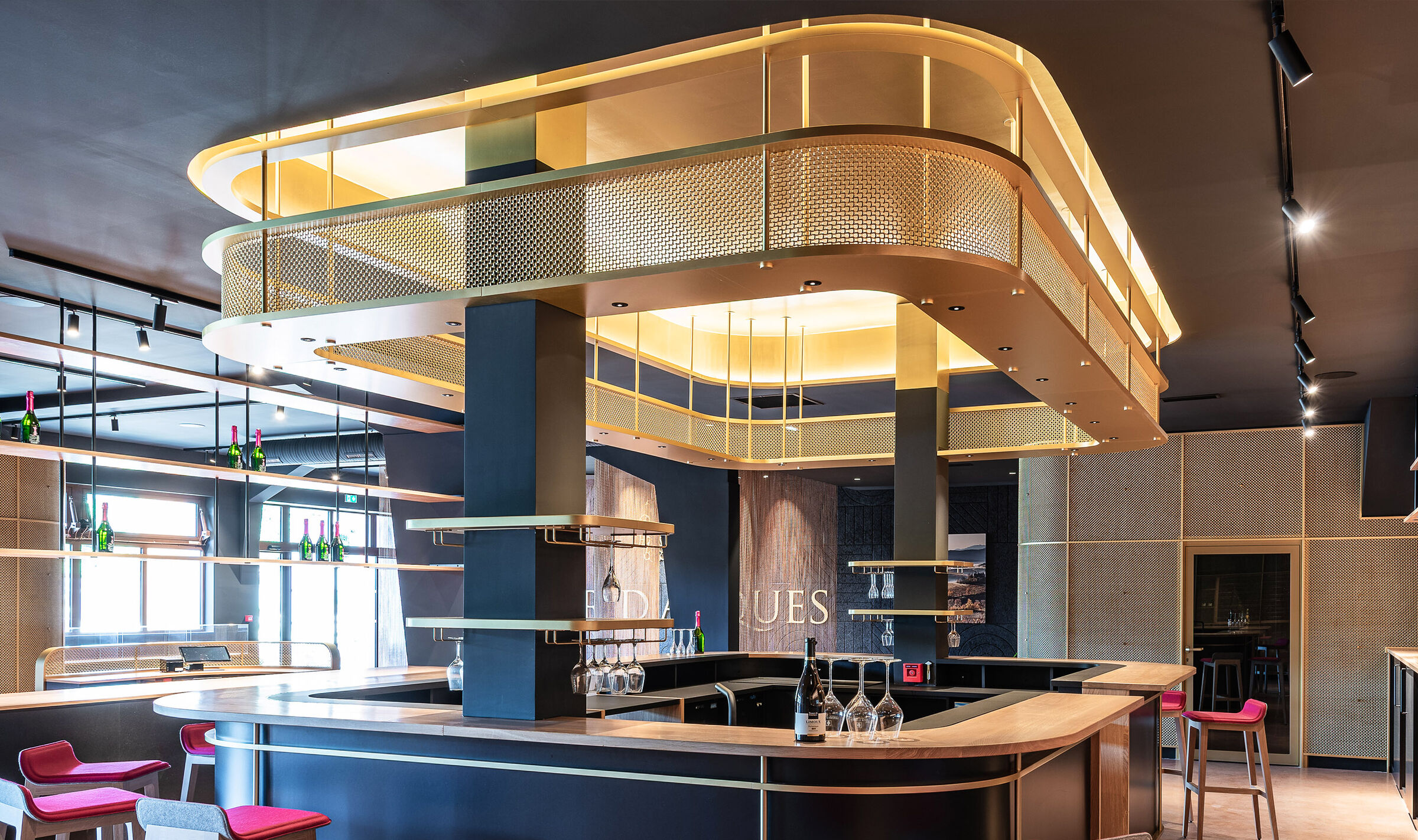 A contemporary wine tasting space features M22-83 brass woven wire mesh as a ceiling gantry that forms a sculptural canopy above the bar.