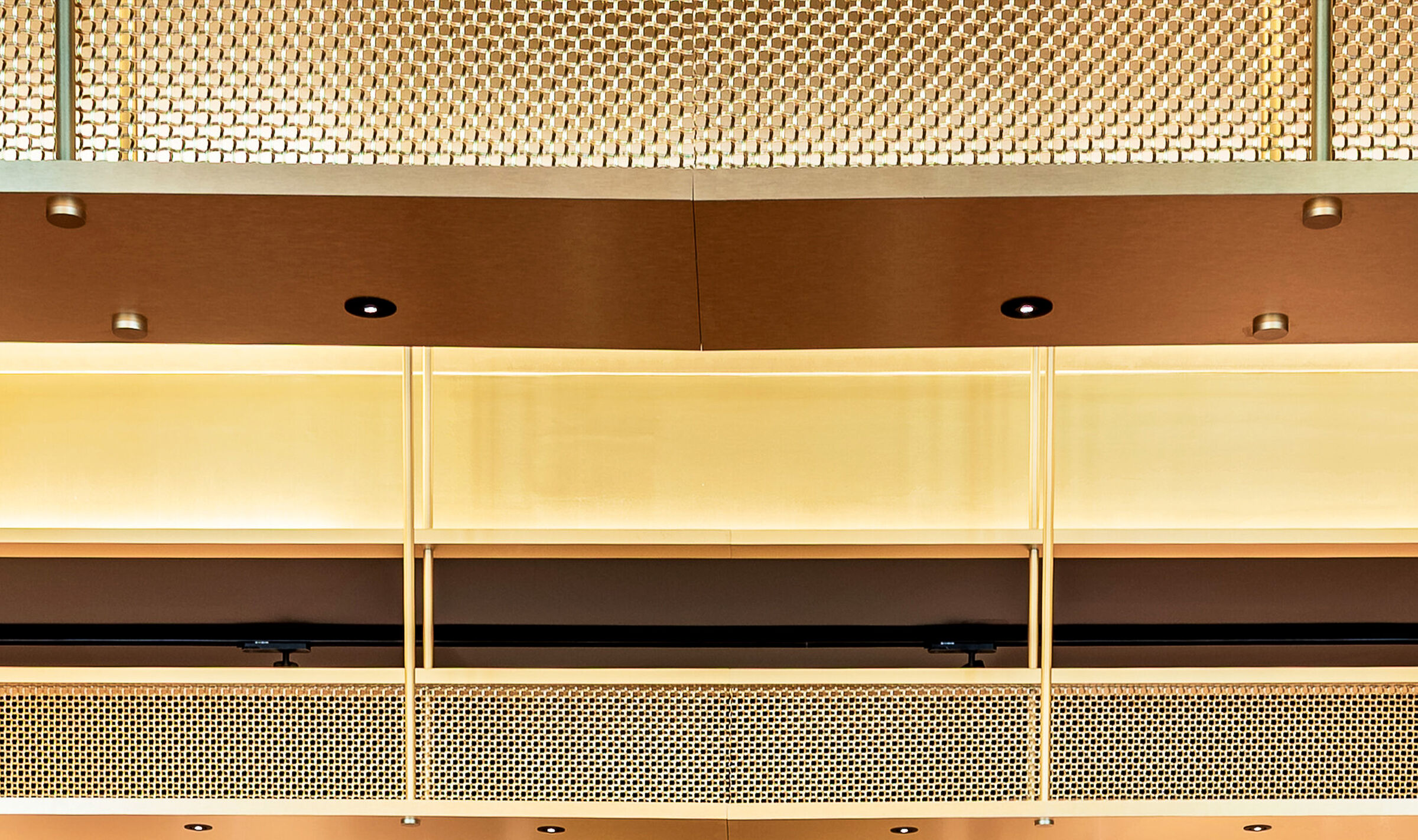 A contemporary wine tasting space features M22-83 brass woven wire mesh as a ceiling gantry that forms a sculptural canopy above the bar.