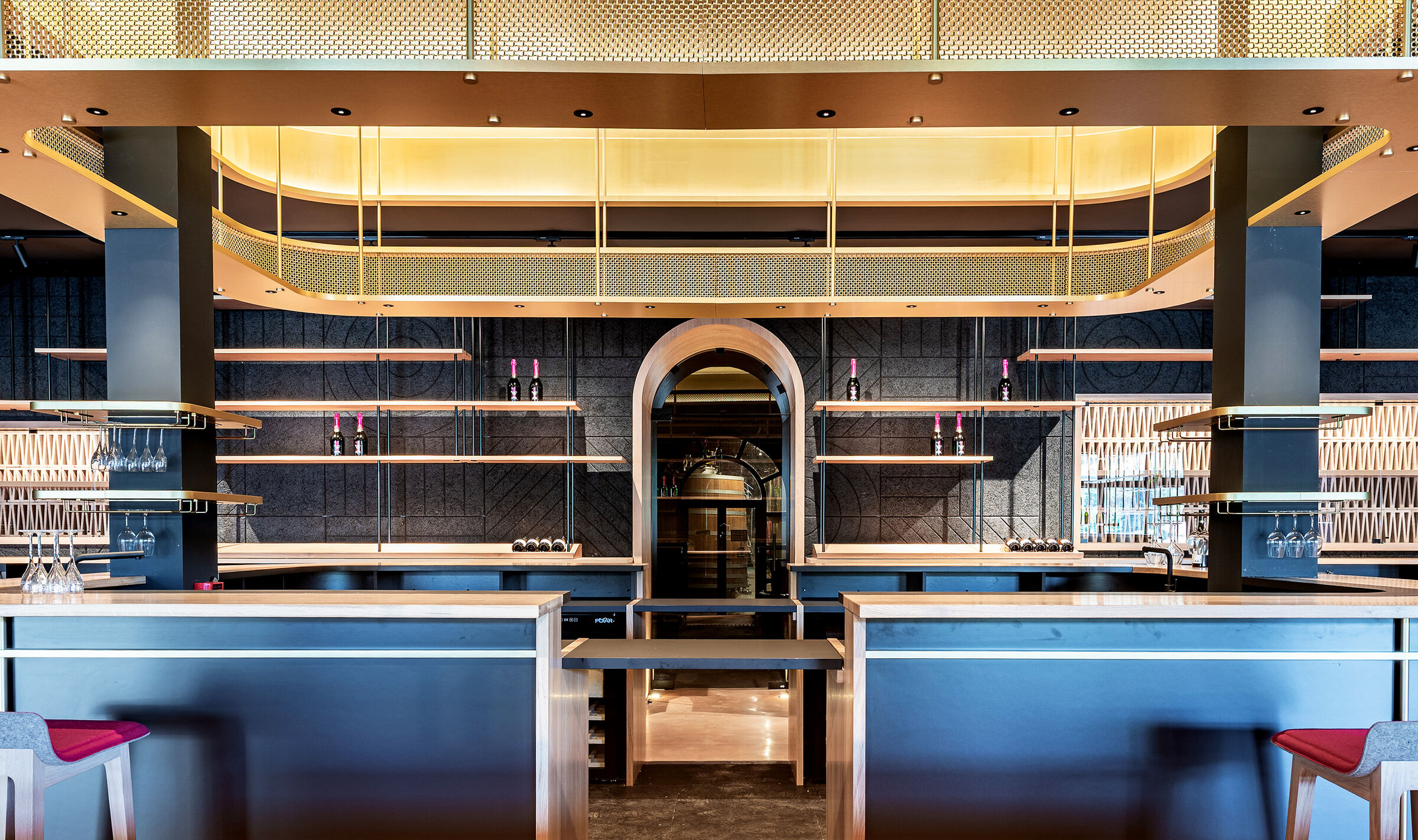 A contemporary wine tasting space features M22-83 brass woven wire mesh as a ceiling gantry that forms a sculptural canopy above the bar.