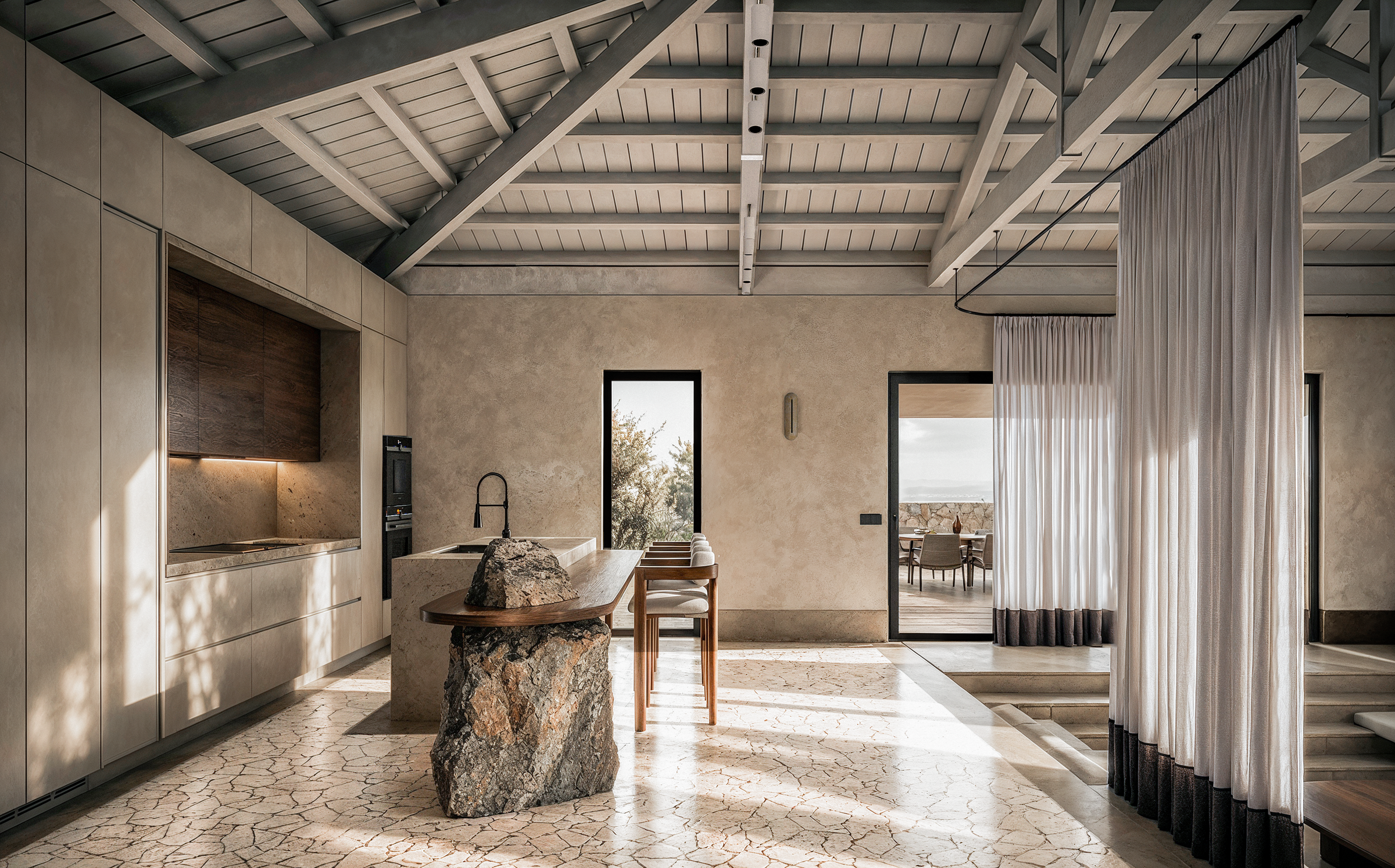 A contemporary kitchen and dining space in Karpathos, where sculptural stone elements, natural textures, and traditional architectural features establish a dialogue between heritage and modern living.