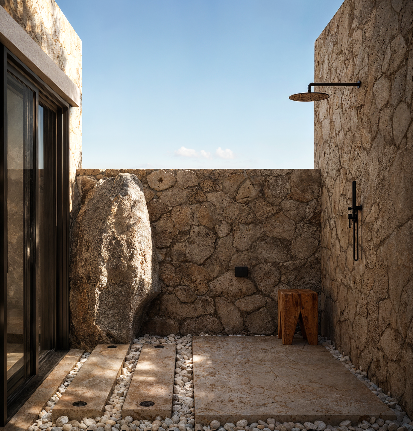An intimate outdoor shower surrounded by natural stone walls reflects the simplicity of traditional Karpathian architecture and its connection to the Mediterranean landscape.
