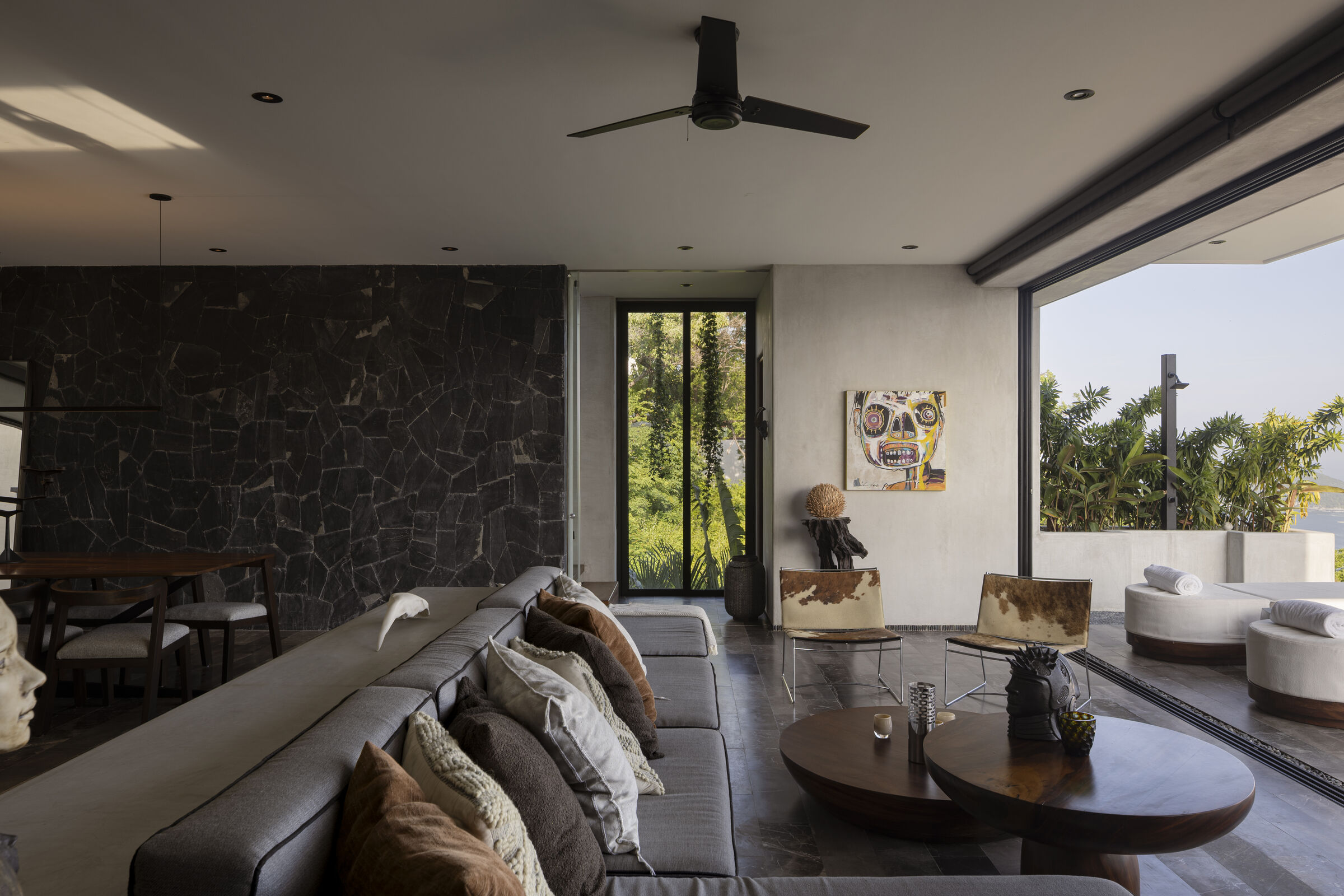 The main living space opens completely to the terrace, framing distant views of the bay and the Pacific Ocean.