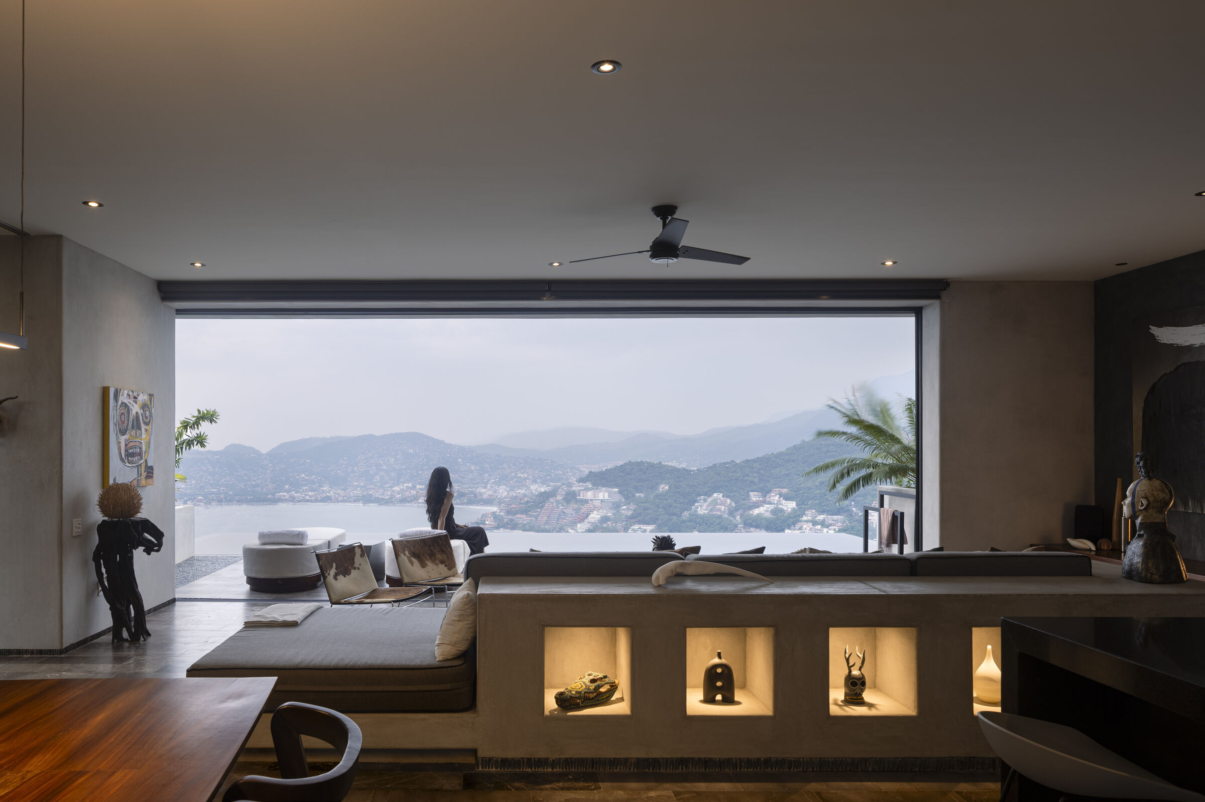 A panoramic opening transforms the bay into a living backdrop, while illuminated niches showcase the homeowners’ art collection.