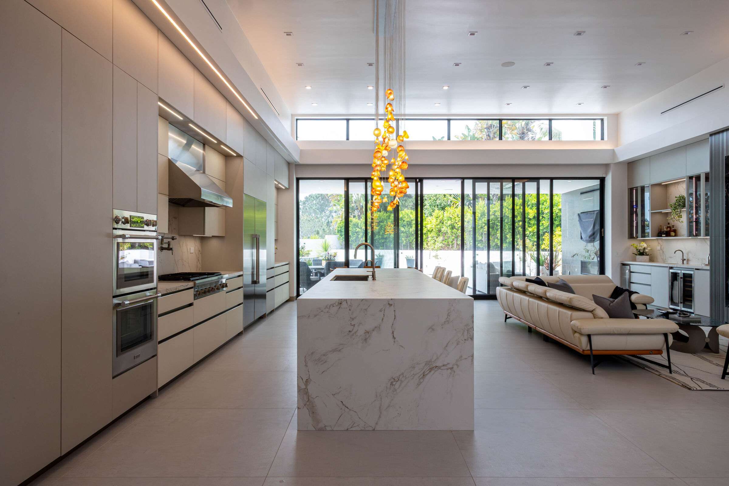 A bespoke glass chandelier connects the open kitchen and living spaces through light and color.