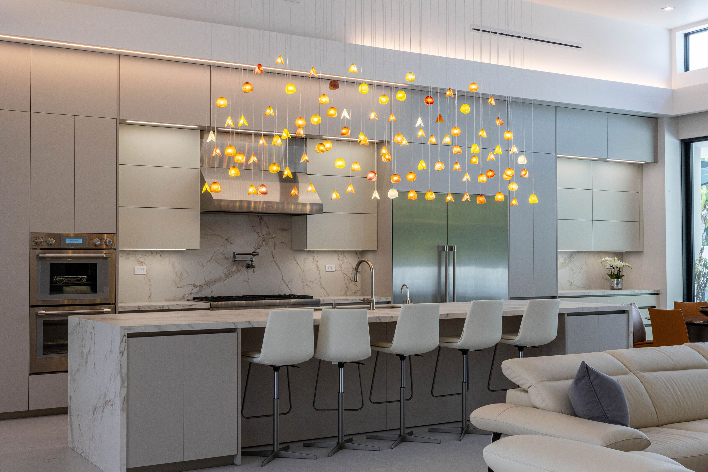 Wide view of the custom chandelier spanning the kitchen island in this contemporary open-plan home.