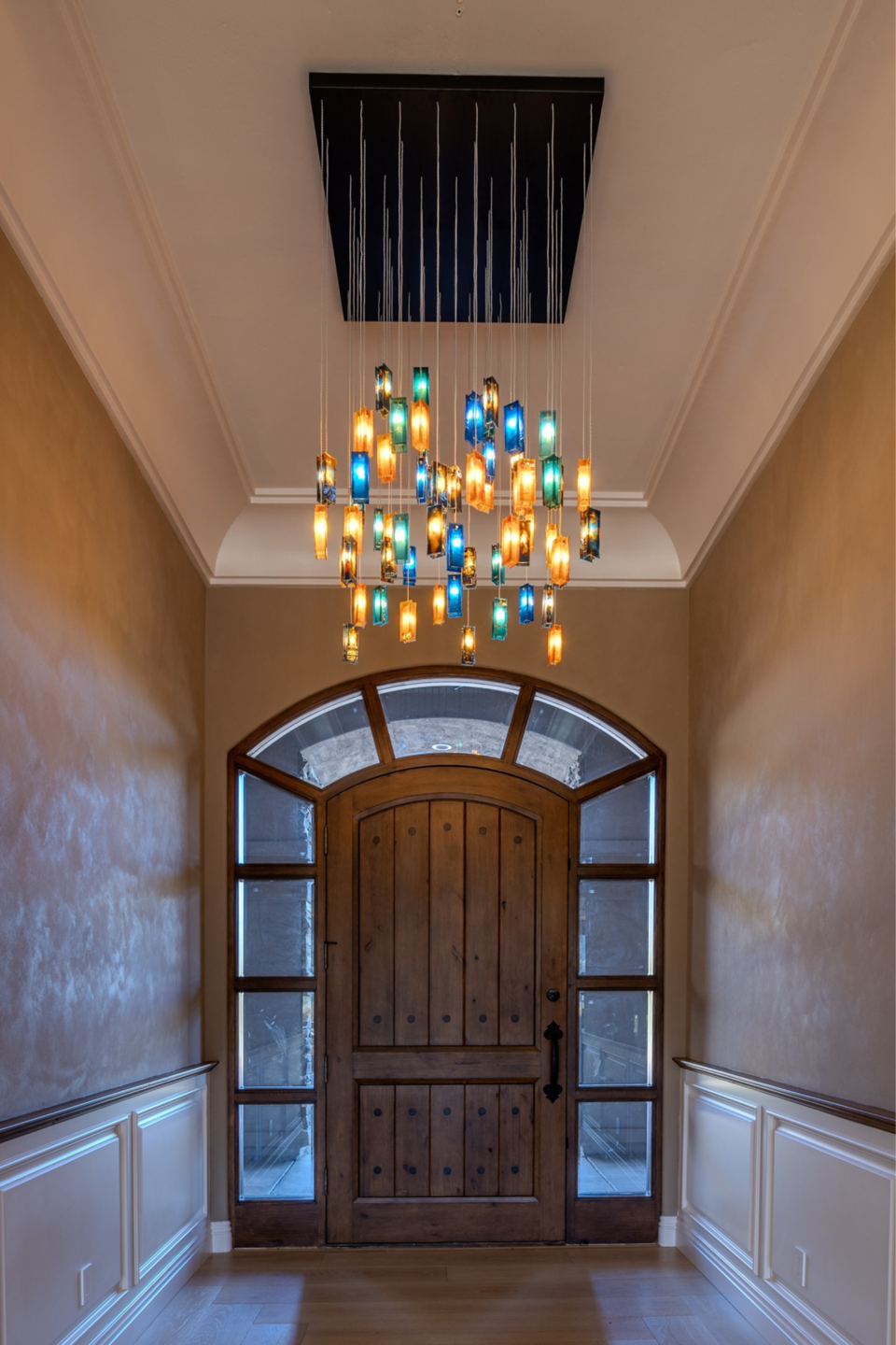 Custom Gleams chandelier creating a dramatic vertical composition in the double-height entrance.