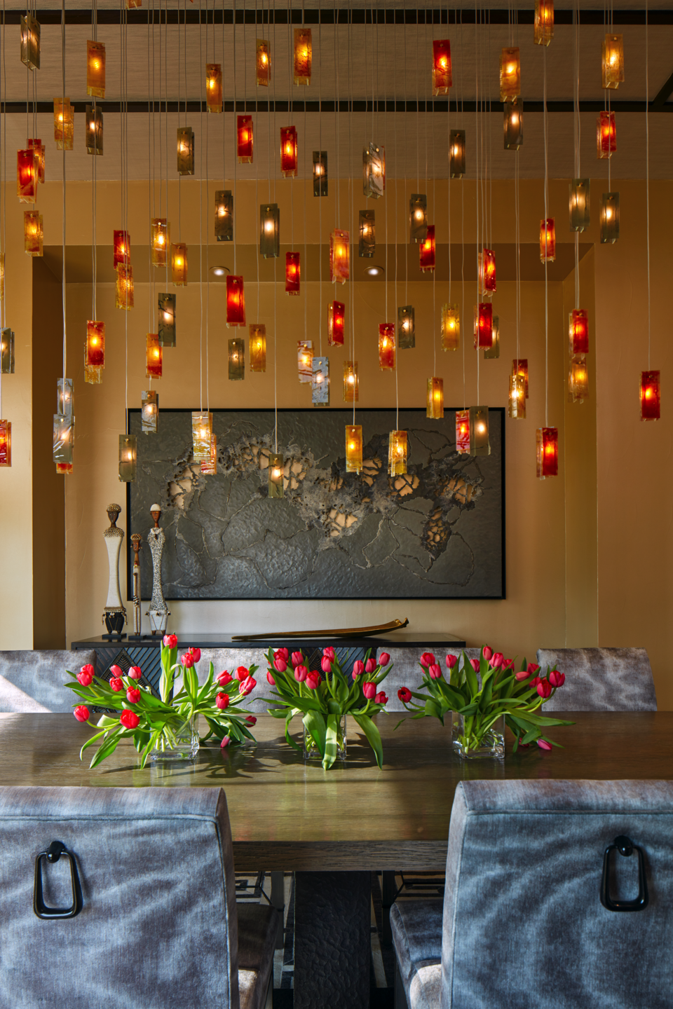 Handcrafted glass chandelier with warm amber, red and clear glass pendants above the dining table.