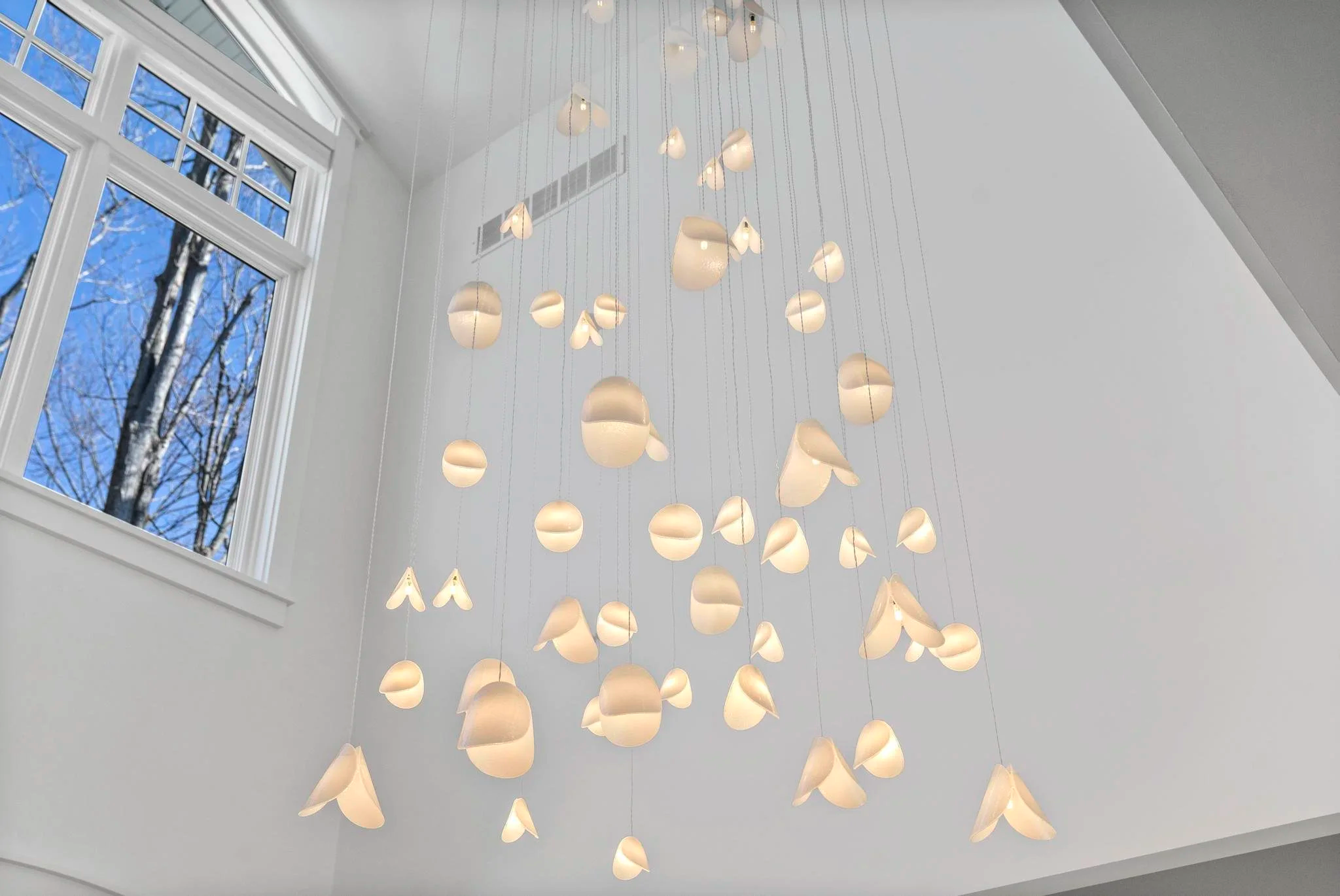 Custom white glass lighting suspended at varying heights, emphasizing the vertical architecture of the foyer.