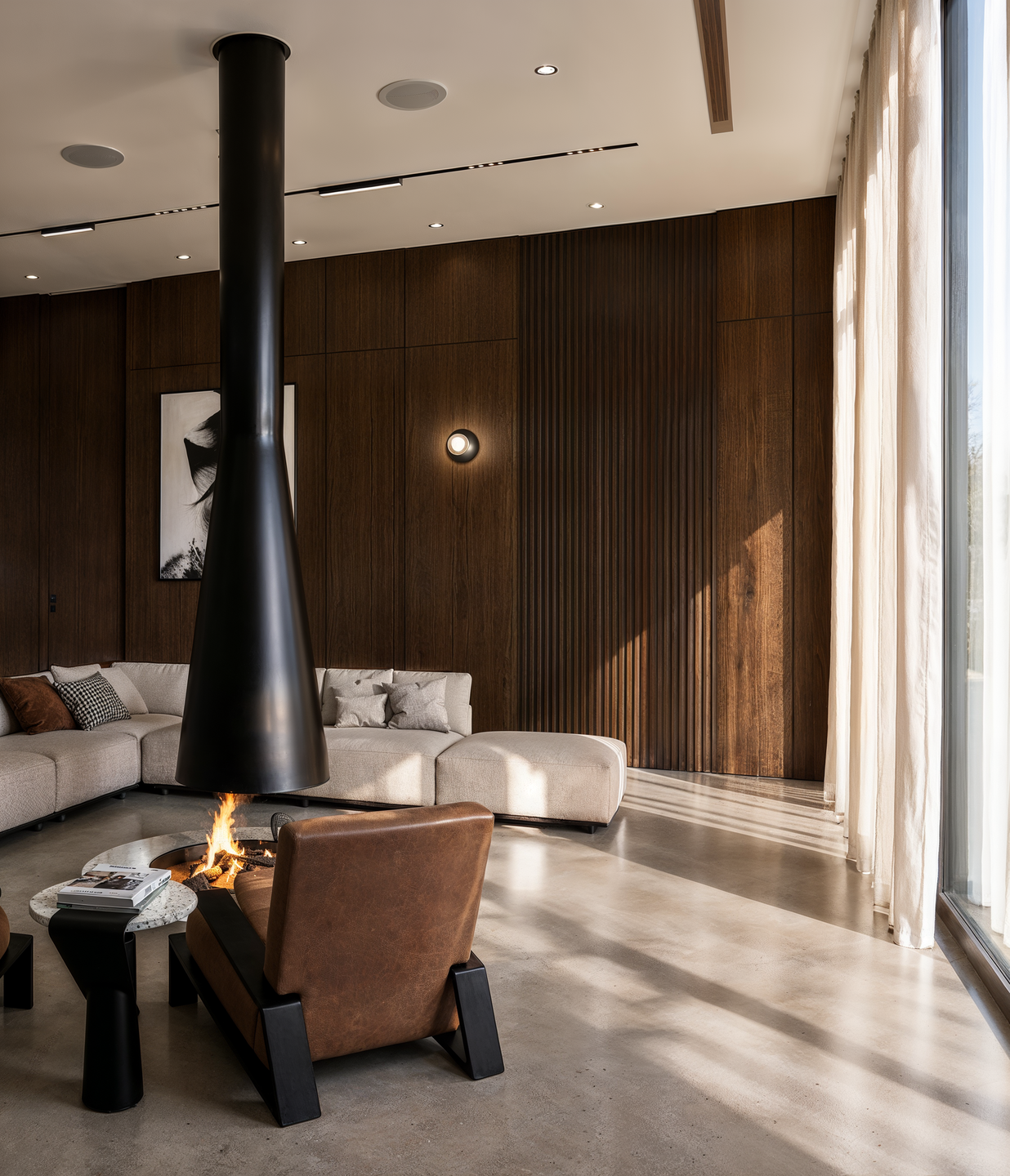 The suspended fireplace becomes the architectural centerpiece of Villa Estia, defining a contemporary gathering space through sculptural geometry, dark timber surfaces, and natural daylight.