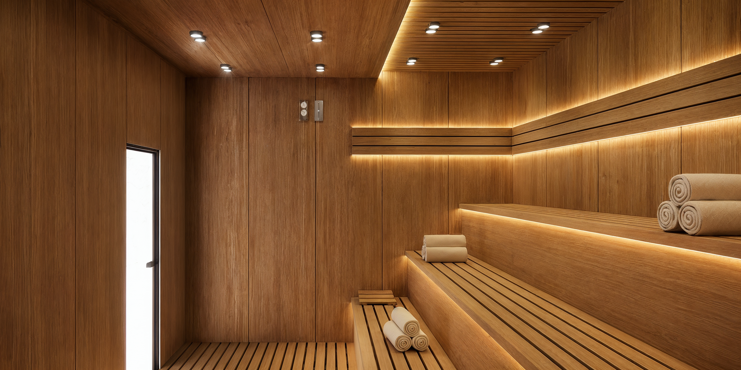 Continuous timber surfaces, precisely integrated seating, and concealed lighting define a minimalist sauna interior focused on material warmth and spatial simplicity.