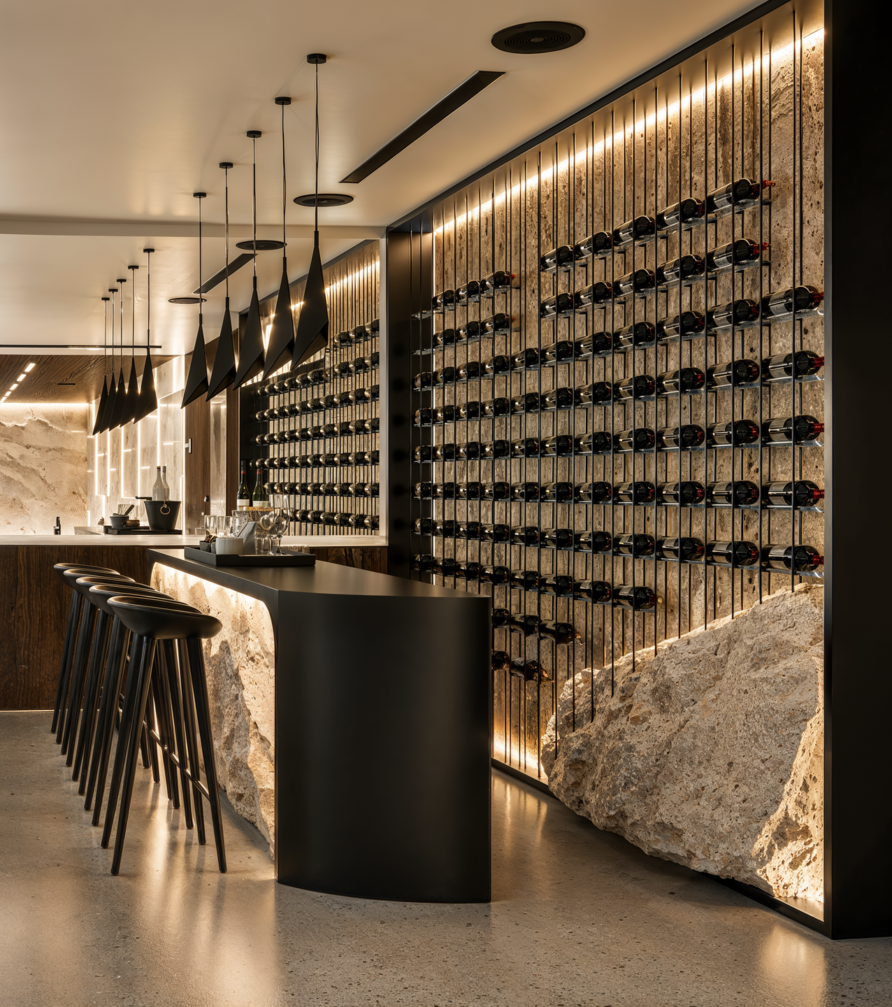 A bespoke wine display transforms the private bar into a distinctive entertainment space, combining natural stone, sculptural lighting, and refined material contrasts.