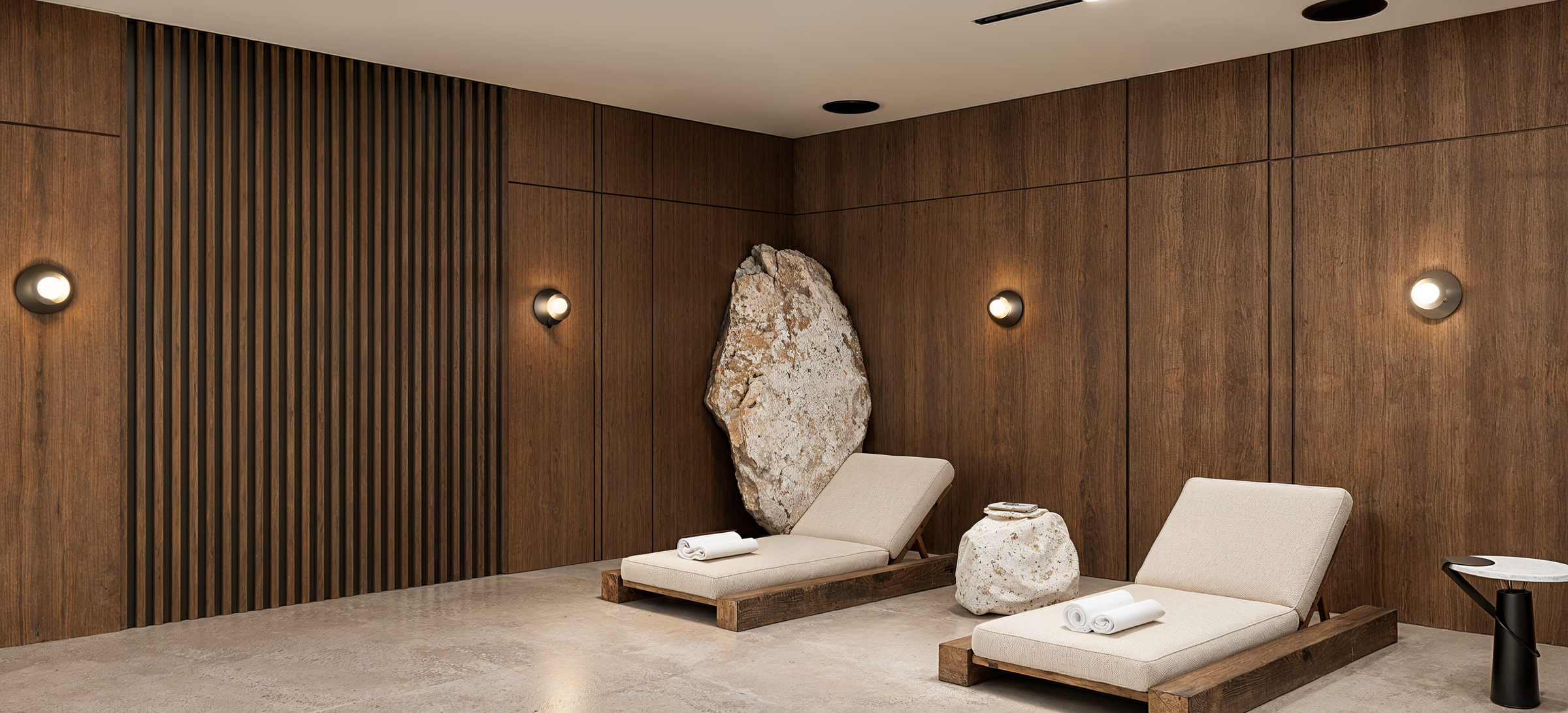The wellness lounge combines natural stone flooring, warm timber surfaces, and minimal furnishings to create a tranquil setting adjacent to the indoor swimming pool.